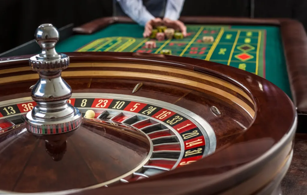 Roulette and piles of gambling chips on a green table in casino. Man hand over casino chips – bet.