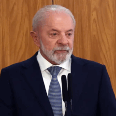 Foto do presidente Lula em discurso, vestindo terno azul escuro e gravata azul clara, diante de painel de madeira. A imagem ilustra o artigo sobre sua fala de que a eleição será uma disputa entre a Faria Lima e o povo, simbolizando o embate entre política e mercado financeiro.
