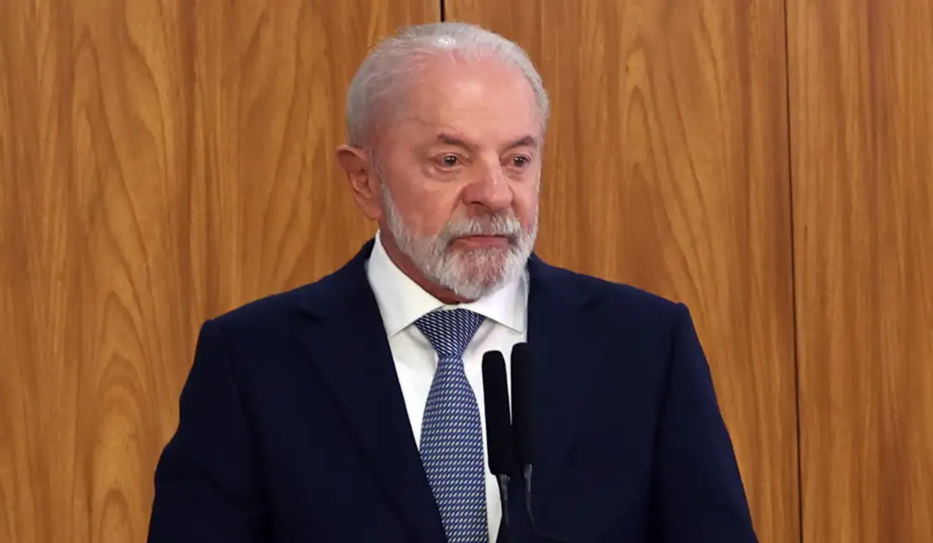 Foto do presidente Lula em discurso, vestindo terno azul escuro e gravata azul clara, diante de painel de madeira. A imagem ilustra o artigo sobre sua fala de que a eleição será uma disputa entre a Faria Lima e o povo, simbolizando o embate entre política e mercado financeiro.