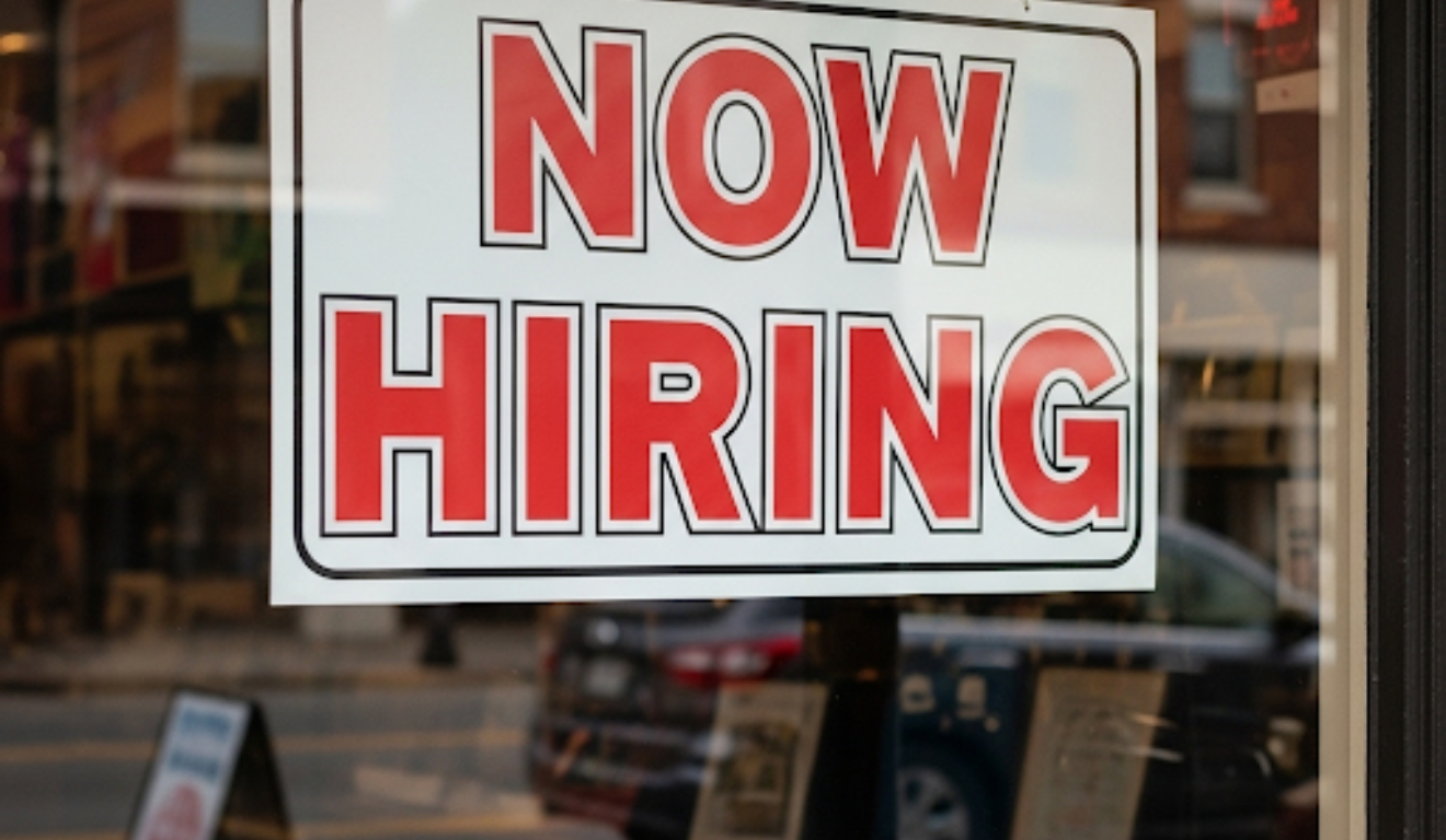 Placa "Now Hiring" em janela de loja nos EUA, refletindo a importância do mercado de trabalho americano para o calendário econômico e o payroll. Placa "Now Hiring" em janela de loja nos EUA, refletindo a importância do mercado de trabalho americano para o calendário econômico e o payroll.