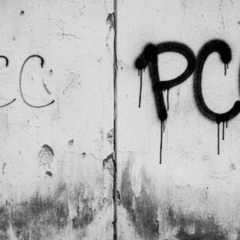 Foto em preto e branco de um muro com a pichação da sigla PCC.