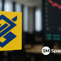 Imagem do logotipo do Banco do Brasil, BB, em um ambiente de escritório. Representa a queda da ação BBAS3 por conta de notícias sobre política.