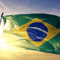 Bandeira do Brasil tremulando com céu azul e sol. Símbolo do crescimento do PIB brasileiro.