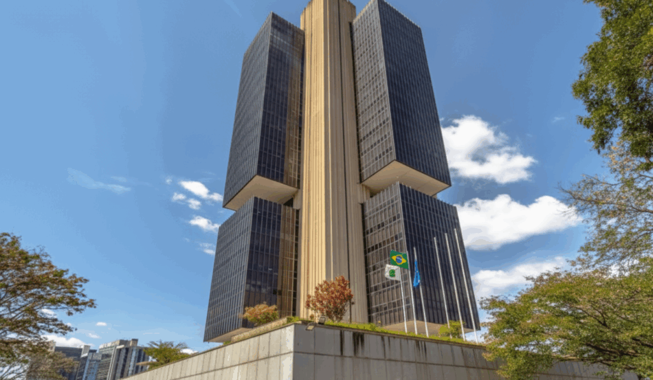 Prédio do Banco Central do Brasil em Brasília em um dia ensolarado, visto de baixo, com céu azul e árvores ao redor. Prédio do Banco Central do Brasil em Brasília em um dia ensolarado, visto de baixo, com céu azul e árvores ao redor.