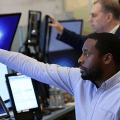 Dois traders em frente a múltiplos monitores analisando dados financeiros durante a venda de bônus globais.