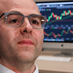 Stephen Miran, diretor do Federal Reserve, com gráficos de mercado ao fundo, discutindo política de juros.