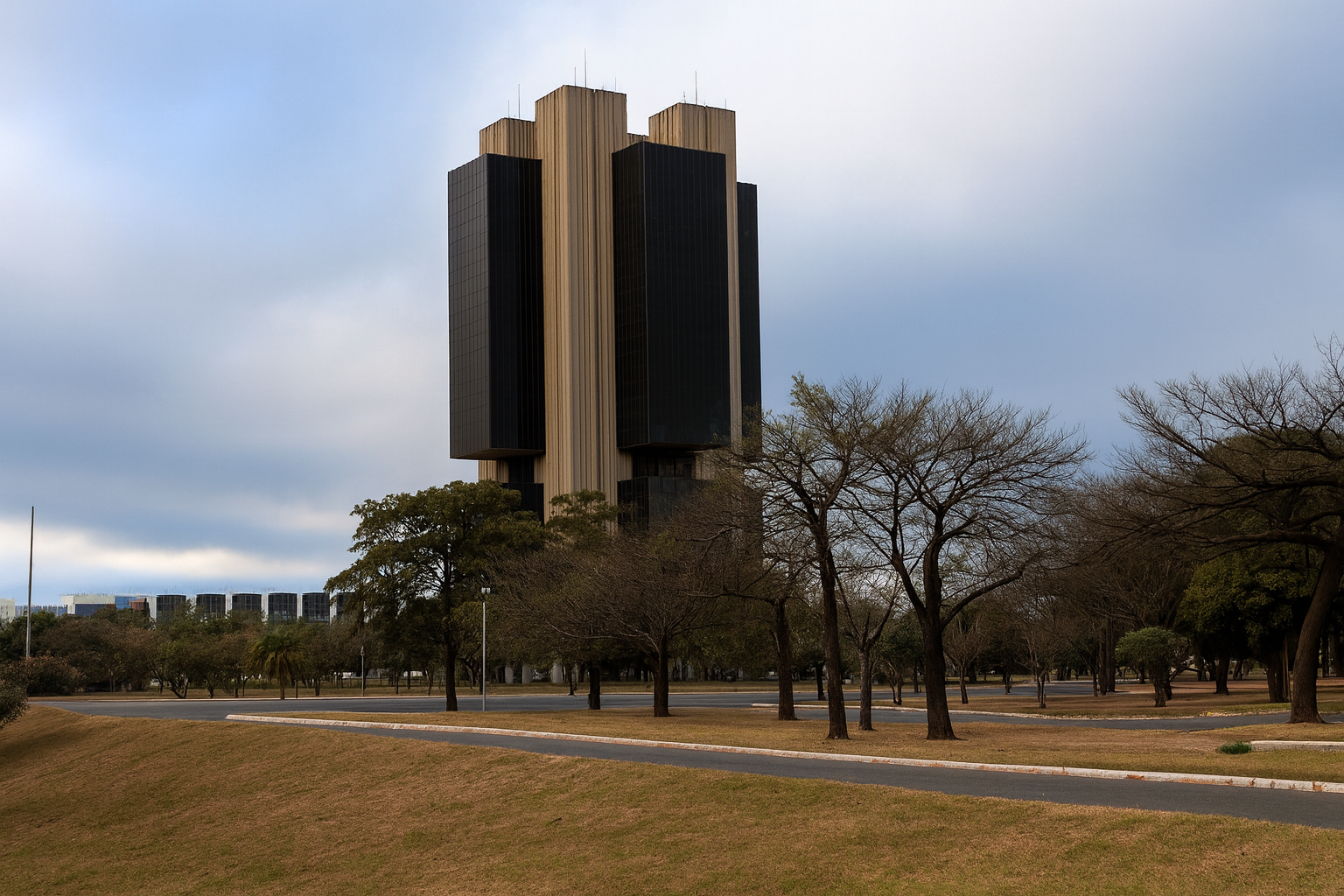Fotografia do edifício-sede do Banco Central do Brasil, uma torre de arquitetura brutalista em tons de cinza e preto, cercada por gramado seco e árvores sob um céu nublado em Brasília