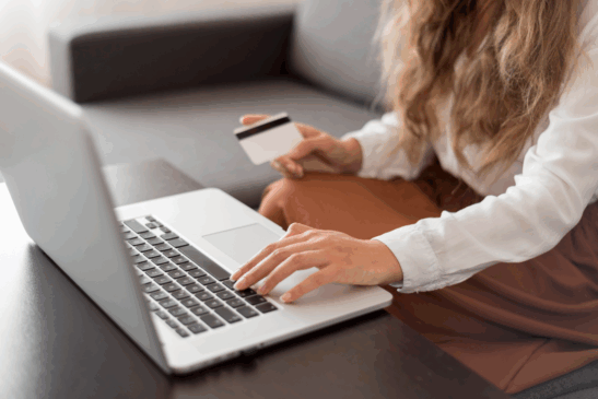 Mulher usando notebook e segurando cartão de crédito enquanto faz compras online