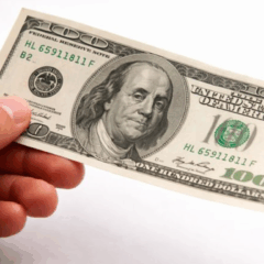 M&atilde;o masculina segurando uma nota de 100 d&oacute;lares, representando a queda do d&oacute;lar frente ao real no encerramento do ano