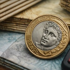 Moeda de um real sobre c&eacute;dulas brasileiras ao lado de calculadora, simbolizando contas p&uacute;blicas e o Or&ccedil;amento de 2026